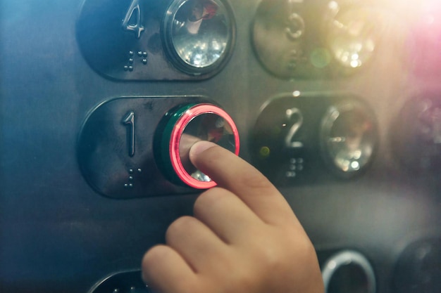 Mano de primer plano de un niño pequeño presionando el botón del piso número uno en un ascensor moderno