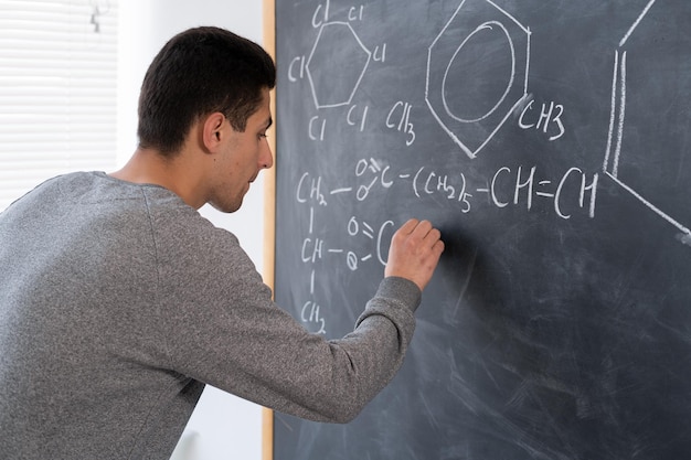 Foto mano de profesor de química árabe con tiza dibujando fórmulas y elementos signos y símbolos de química concepto de educación químico