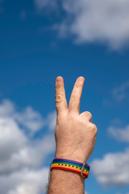 Mano con pulsera de arco iris del orgullo gay haciendo un signo de paz