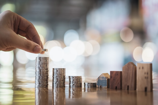 Mano que elige la fila del dinero de la moneda en la tabla de madera y la mini casa de madera,