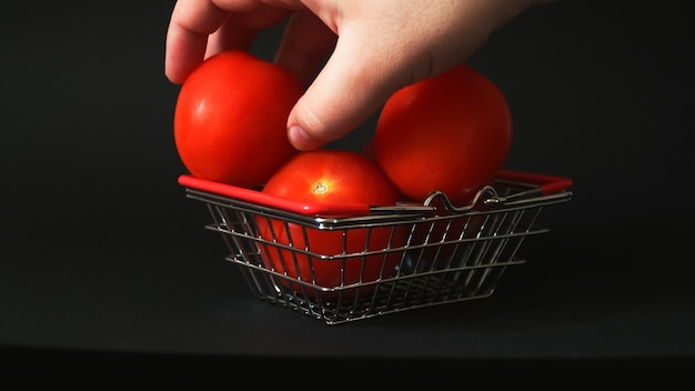 Mano que un hombre extiende y recoge tomates en una canasta pequeña para la tienda