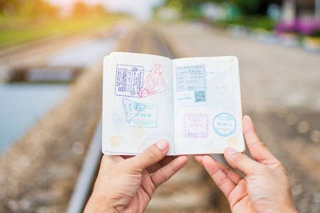 Foto mano que lleva a cabo sellos de la inmigración de la demostración del pasaporte en pasaporte con el fondo ferroviario.