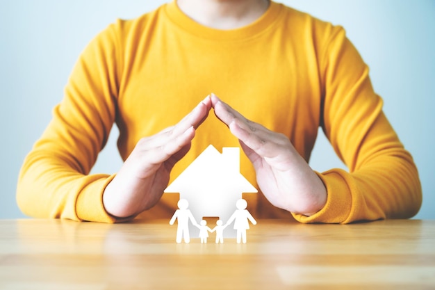 Foto mano que protege a las personas de la familia y la casa en la mesa de madera concepto de salud y seguro de vida