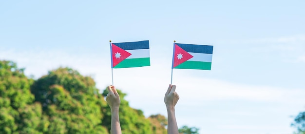 Mano que sostiene la bandera de Jordania en el fondo de la naturaleza Día de la Independencia de Jordania y conceptos de celebración feliz