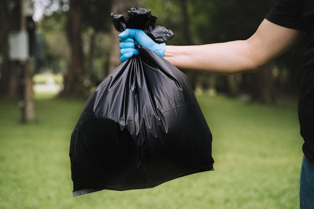 La mano que sostiene una bolsa de basura negra la está poniendo en el bote de basura