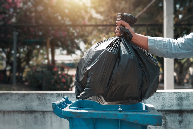 Foto mano que sostiene la bolsa de basura negro poniendo en la basura