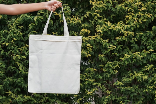 Foto mano que sostiene la bolsa de tela en el fondo de la hoja verde