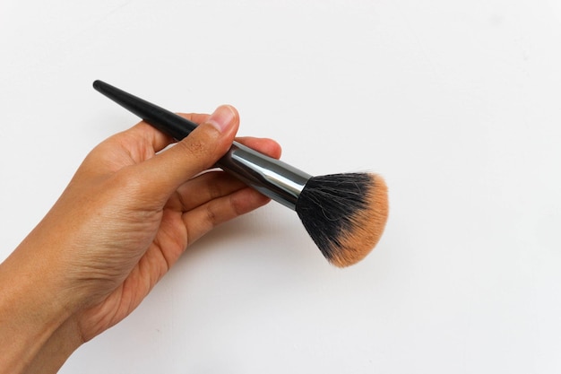 Foto mano que sostiene el cepillo cosmético para maquillaje aislado sobre fondo blanco