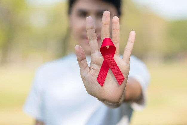 Mano que sostiene la cinta roja para apoyar a las personas que viven y enferman. Concepto de salud y sexo seguro. Diciembre Día mundial del sida y mes de concientización sobre el cáncer de mieloma múltiple