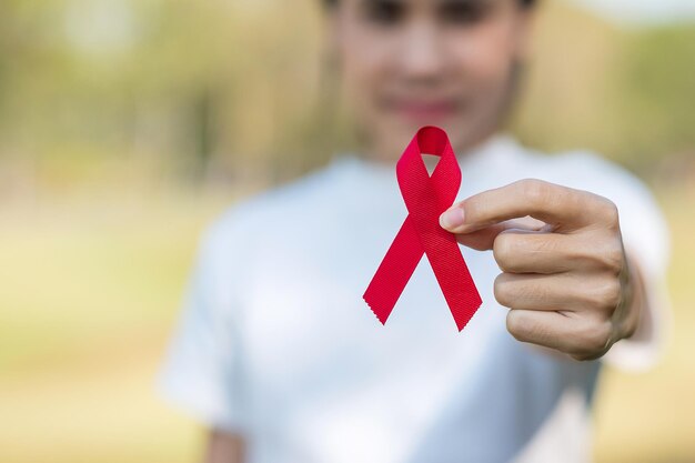Mano que sostiene la cinta roja para apoyar a las personas que viven y enferman. Concepto de salud y sexo seguro. Diciembre Día mundial del sida y mes de concientización sobre el cáncer de mieloma múltiple
