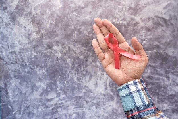 Mano que sostiene la cinta roja del VIH de arriba hacia abajo