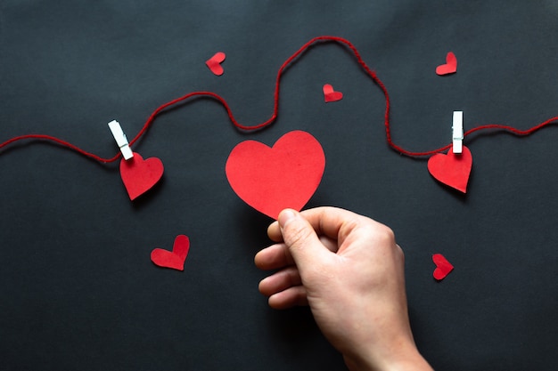 La mano que sostiene un corazón negro sobre fondo negro, el Día de San Valentín. Lay Flat