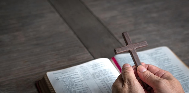 Mano que sostiene la cruz religiosa del crucifijo encima de la biblia santa