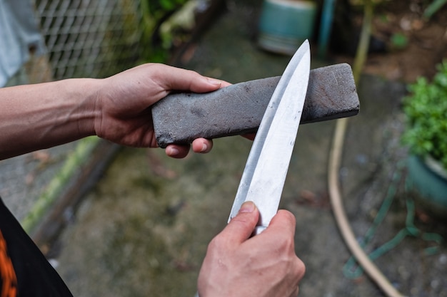 Mano que sostiene el cuchillo y la piedra de afilar para afilar el cuchillo. Cuchillo afilador manual.