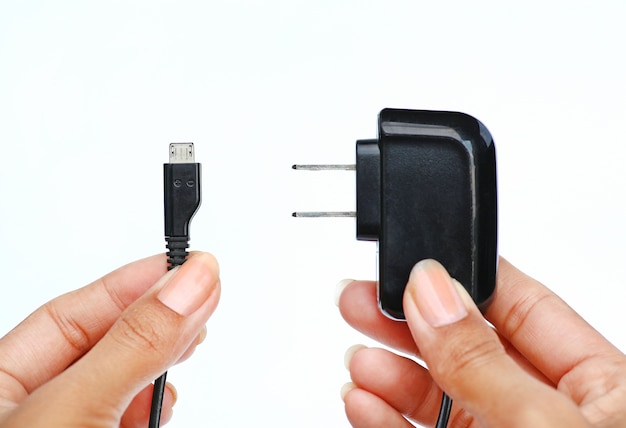 Foto mano que sostiene el enchufe eléctrico y cable micro usb sobre fondo blanco