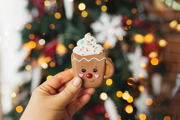 Mano que sostiene la galleta de jengibre de Navidad y decoraciones en el árbol de Navidad, taza de pan de jengibre.