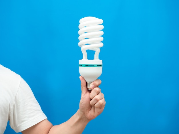 Mano que sostiene la lámpara de luz energía ahorrar fondo azul aislado tiro del estudio