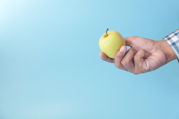 mano que sostiene la manzana verde sobre fondo azul