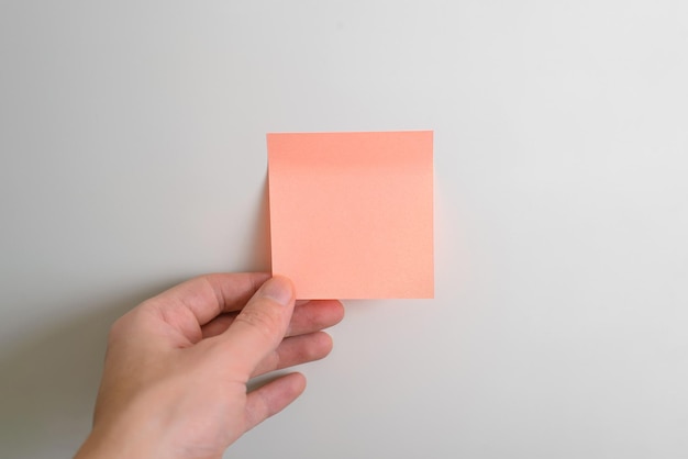 Mano que sostiene la maqueta de la etiqueta engomada en blanco rosa en el primer plano del refrigerador