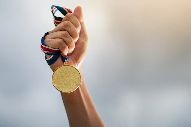 Mano que sostiene la medalla de oro en el cielo