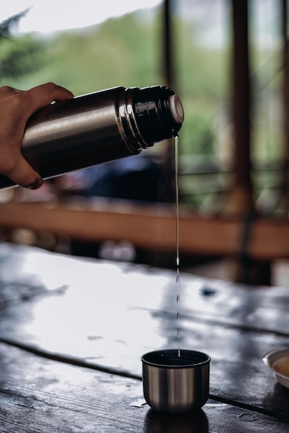 Una mano que sostiene un molinillo de café de acero inoxidable con tapa negra y un recipiente de metal plateado con tapa de metal plateado.