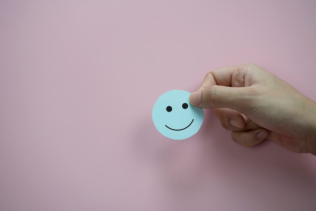 Mano que sostiene el papel de carita feliz verde cortado sobre fondo rosa pastel