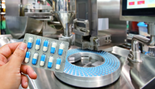 Foto mano que sostiene el paquete de cápsulas azules en la línea de producción de píldoras de medicina, concepto farmacéutico industrial.