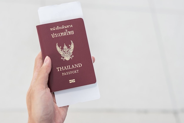 Mano que sostiene el pasaporte de Tailandia y el boleto de embarque.