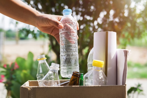 Mano que sostiene el plástico de la botella de basura que pone en la bolsa de reciclaje para limpiar