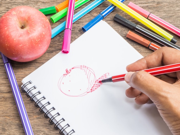 Mano que sostiene la pluma para dibujar la manzana roja