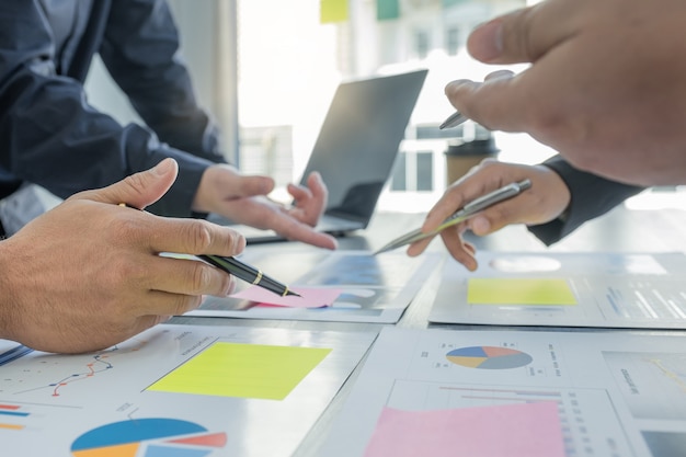 Mano que sostiene la pluma, la reunión del equipo de mujeres empresarias y empresarios para planificar estrategias para aumentar los ingresos comerciales