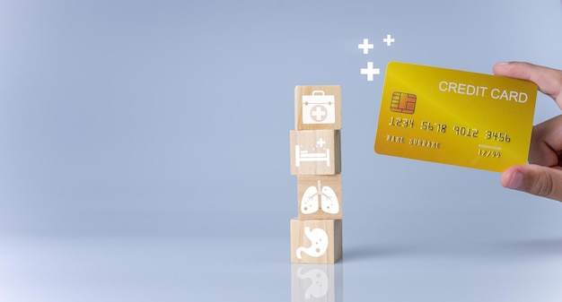 Mano que sostiene la tarjeta de crédito y bloques de cubos de madera apilados con iconos Concepto de salud y medicina