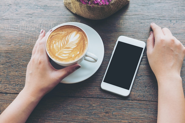 Mano que sostiene la taza de café con teléfono inteligente maqueta