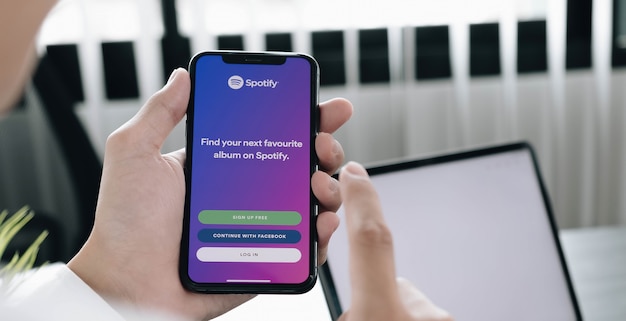 Mano que sostiene un teléfono con la aplicación de spotify, inicie sesión en la pantalla