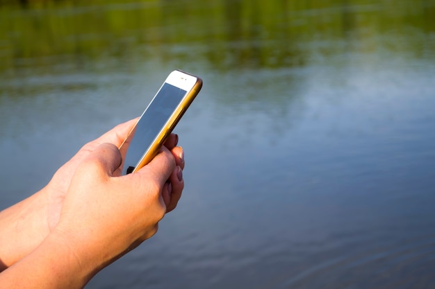 Mano que sostiene el teléfono celular con pantalla en blanco que muestra la aplicación móvil contra la maqueta recortada al aire libre de la playa del mar