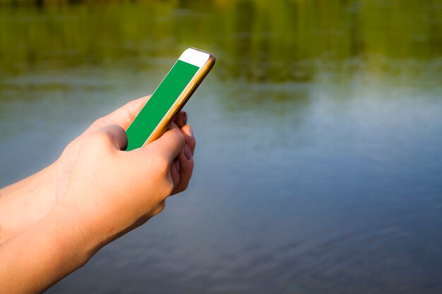 Mano que sostiene el teléfono celular con pantalla en blanco que muestra la aplicación móvil contra la maqueta recortada al aire libre de la playa del mar