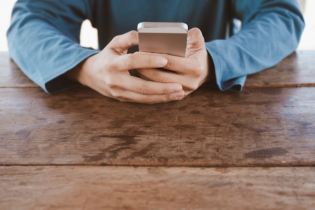 Mano que sostiene el teléfono inteligente en la mesa de madera con espacio de copia