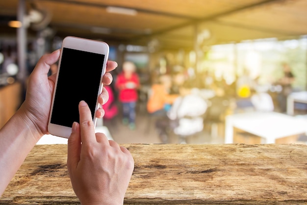 Mano que sostiene el teléfono inteligente móvil con el fondo borroso de la cafetería