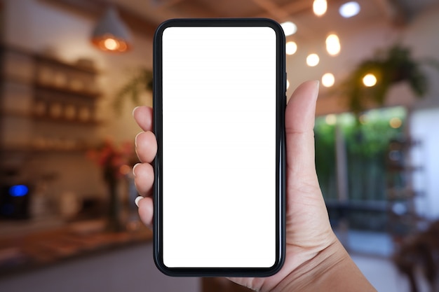 Mano que sostiene el teléfono inteligente con pantalla en blanco para la aplicación en el interior del café