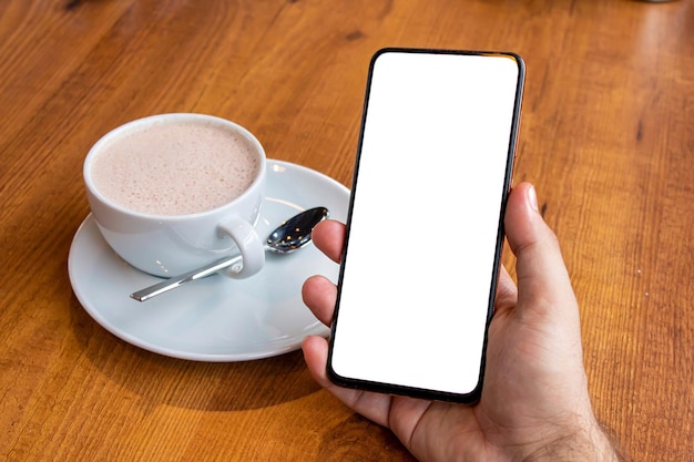 Mano que sostiene el teléfono inteligente con pantalla en blanco en un café. Imagen de la maqueta del teléfono.
