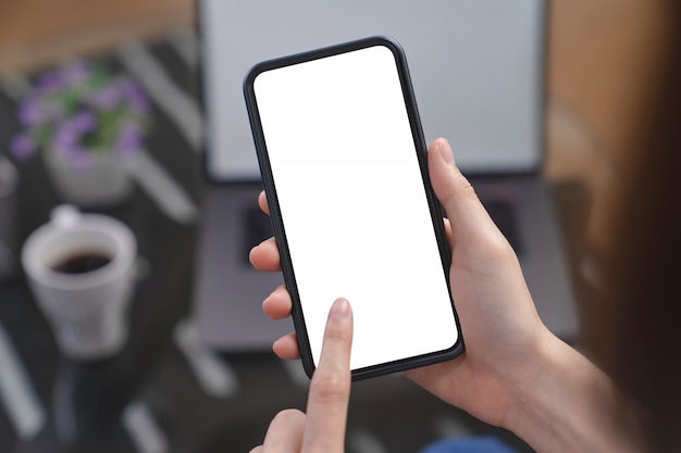 Mano que sostiene el teléfono inteligente de pantalla en blanco en la oficina de escritorio