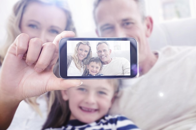 Foto mano que sostiene el teléfono inteligente que se muestra contra el padre que abraza a su hijo en el sofá