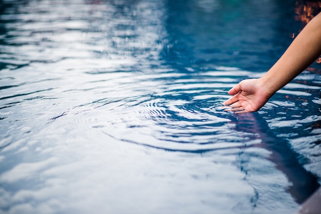 La mano que toca el agua azul. La piscina está limpia y brillante. Con una gota de agua o