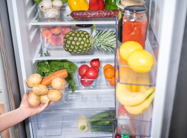 Mano que toma el recipiente con verduras de la nevera