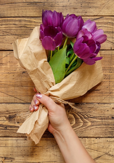 Mano con ramo de tulipanes morados en papel artesanal sobre mesa de madera de cerca