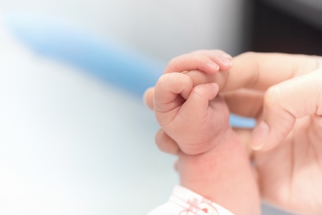 Foto mano recién nacida con dedo de la madre en concepto de hospital, bebé y salud