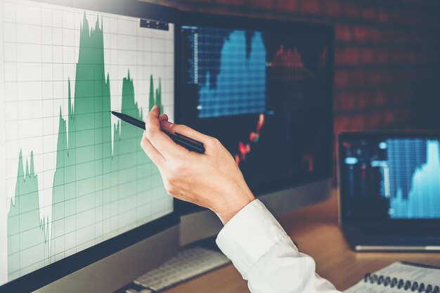 Mano recortada apuntando hacia el gráfico en las pantallas de la computadora