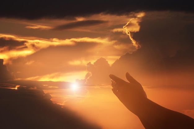 Mano recortada contra el cielo nublado durante la puesta de sol