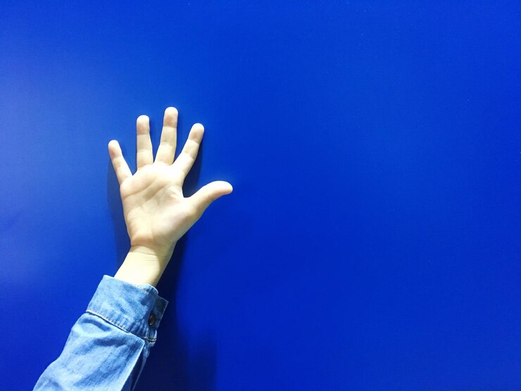 Foto mano recortada contra la pared azul