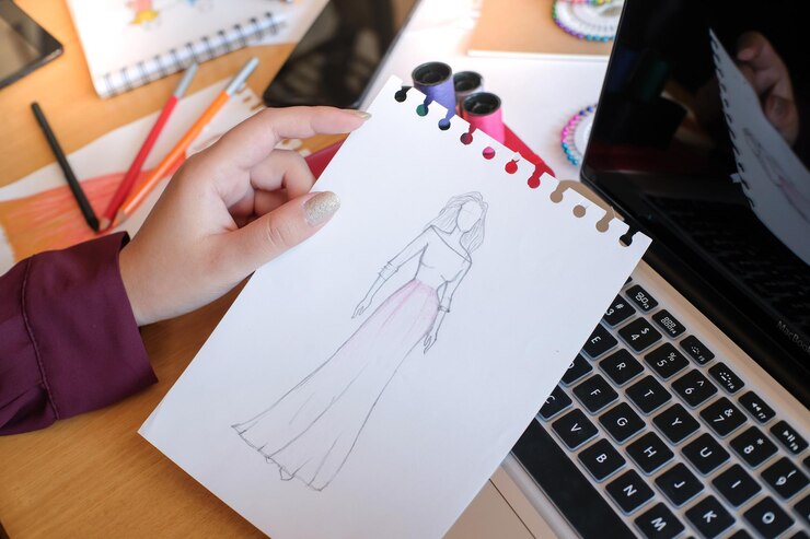 Foto mano recortada de un diseñador de moda sosteniendo un boceto en el estudio
